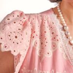 Close-up of a pink lace blouse with floral embroidery and a pearl necklace.