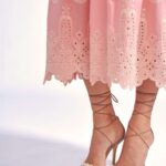 Woman wearing a pink lace dress with pearl-embellished nude high-heeled sandals, ankles wrapped in thin straps.