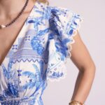 Close-up of a blue-and-white printed dress with a ruffled lace sleeve and gold bracelet visible on the wrist.