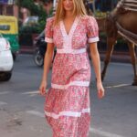 Woman in a pink floral lace dress with white trim walking on a city street, with a camel visible in the background.