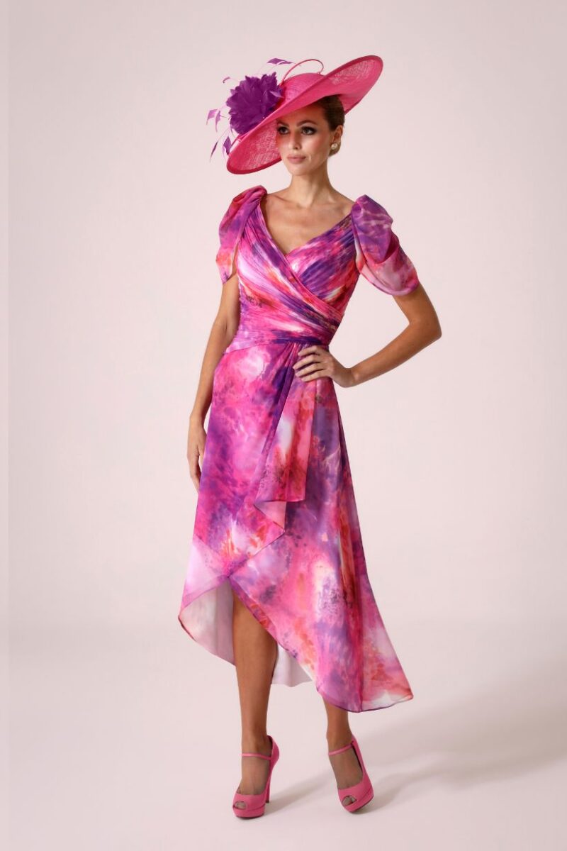 Model in a pink and purple tie-dye wrap dress with a matching wide-brim pink hat and pink heels, posing with hand on hip.