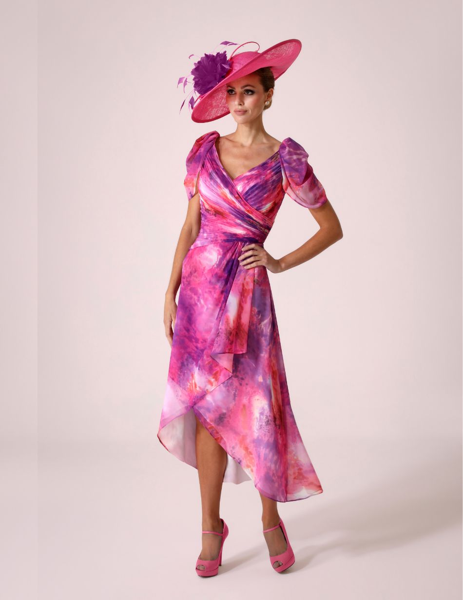 Model in a pink and purple tie-dye wrap dress with a matching wide-brim pink hat and pink heels, posing with hand on hip.
