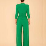 Back view of a person wearing a bright green, fitted top with wide-leg pants; hair in a bun against a neutral beige studio background.