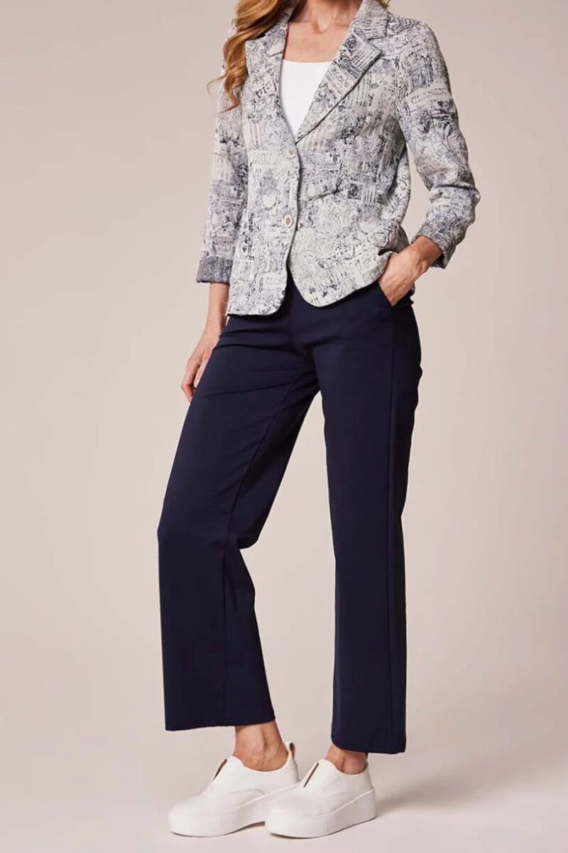 Woman modeling an outfit: snakeskin-pattern blazer over a white top, navy ankle-length pants, and white slip-on sneakers, with one hand in her pocket.