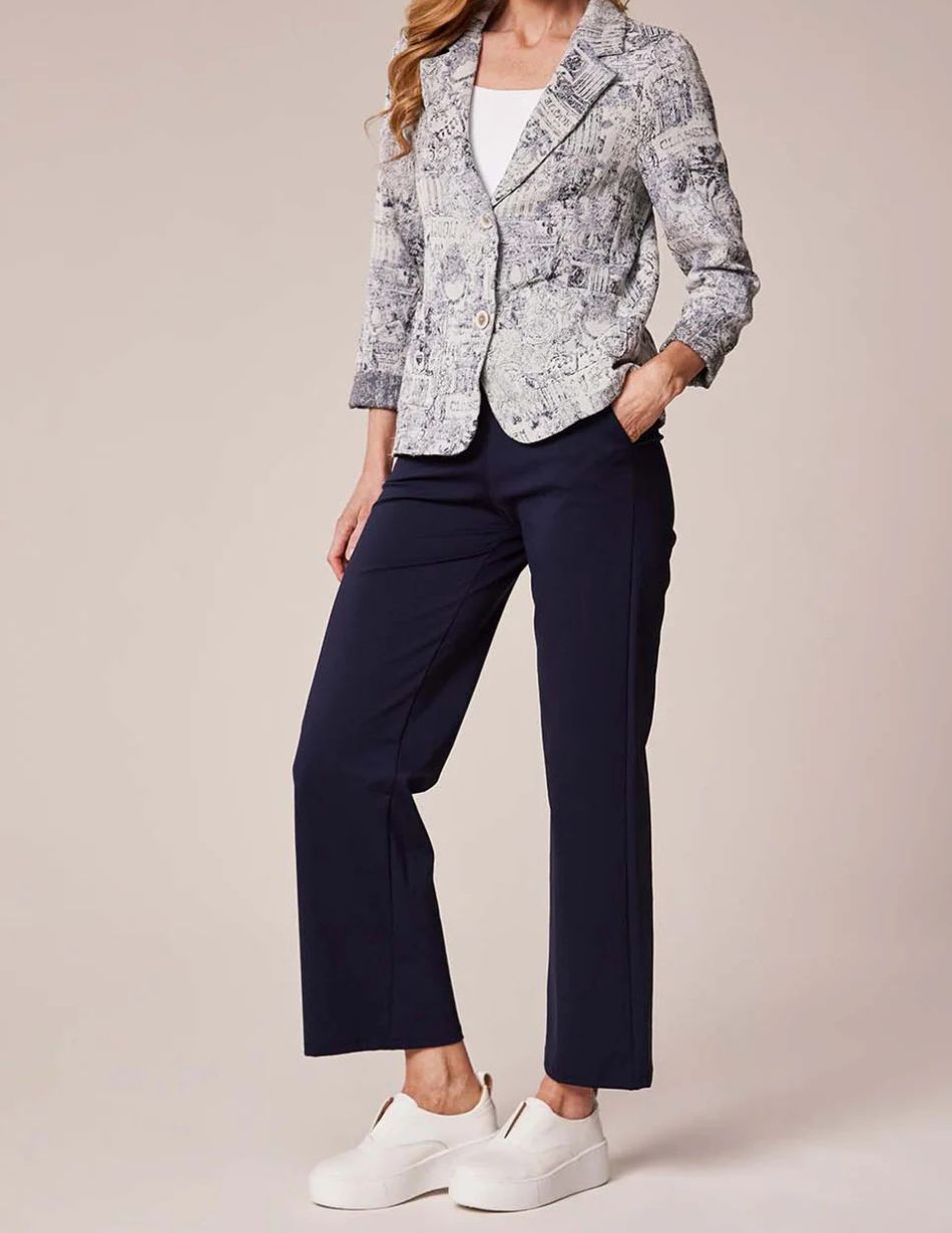 Woman modeling an outfit: snakeskin-pattern blazer over a white top, navy ankle-length pants, and white slip-on sneakers, with one hand in her pocket.
