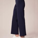 Side view of a person wearing navy wide-leg pants with a white top and white platform sneakers.