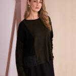Woman modeling a loose olive green and black color-block sweater with a quilted side panel.