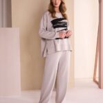 Model wearing a beige oversized sweatshirt and matching wide-leg pants with a black brushstroke graphic, in a soft pastel studio setting.