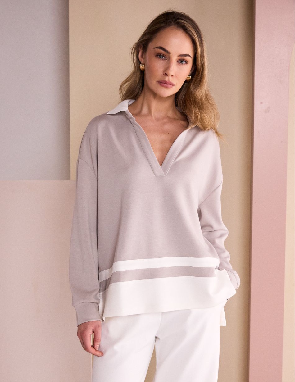 NAW26134 Front Model wearing an oversized taupe sweater with a white hem and white pants, standing against a pastel backdrop.