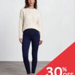 Woman in a cream cable-knit sweater and navy jeans, standing with a diagonal red 30% OFF promotion banner in the bottom right corner.