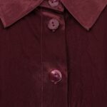 Close-up of a burgundy satin shirt collar with glossy buttons along the placket.
