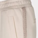 Beige jogger pants with an elastic waistband, a decorative braided side stripe, and a vertical pocket opening visible on the hip.