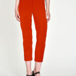 Orange-red cropped pants worn by a model, paired with a white top and brown platform sandals.
